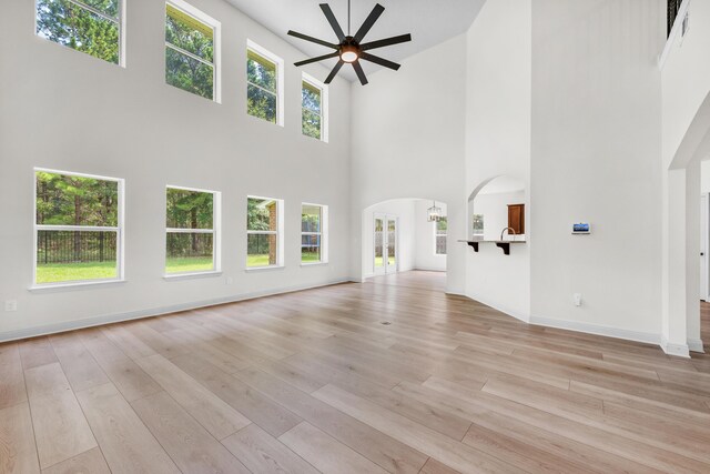 unfurnished living room featuring ceiling fan, light hardwood / wood-style floors, and a high ceiling