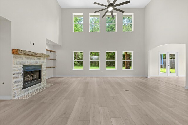 unfurnished living room featuring light hardwood / wood-style floors, a fireplace, a wealth of natural light, and a high ceiling