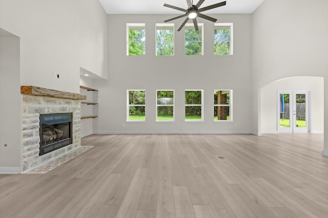 unfurnished living room with light wood-style floors, baseboards, a stone fireplace, and french doors