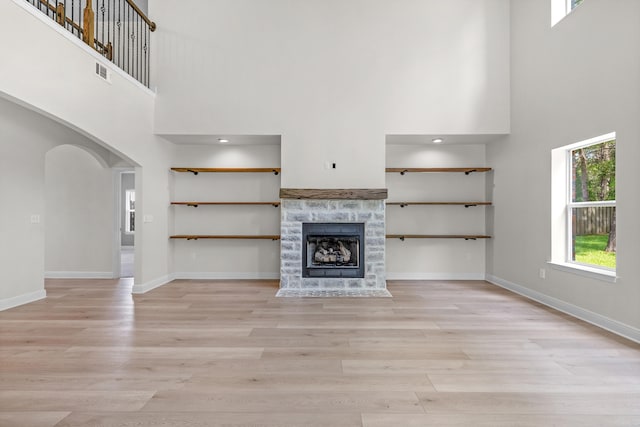 unfurnished living room featuring a stone fireplace, light hardwood / wood-style flooring, and a high ceiling