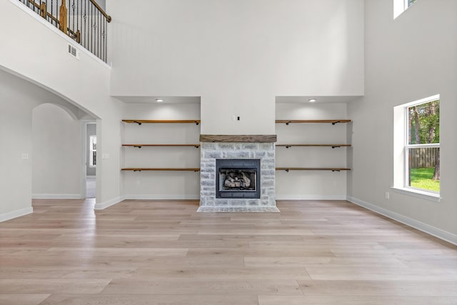 unfurnished living room with arched walkways, a towering ceiling, light wood-style flooring, a tiled fireplace, and baseboards