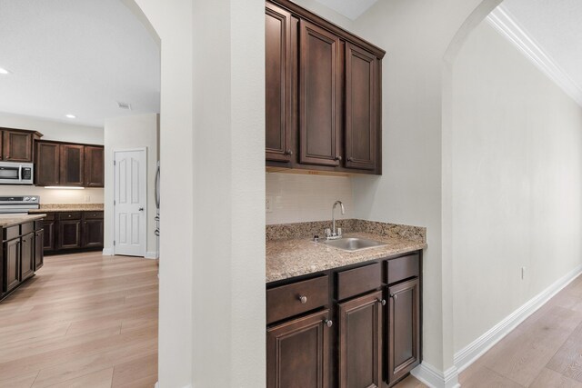 kitchen with light stone counters, light hardwood / wood-style flooring, dark brown cabinets, and sink