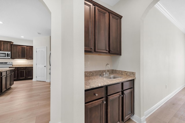 kitchen with arched walkways, dark brown cabinetry, stainless steel appliances, a sink, and light wood finished floors