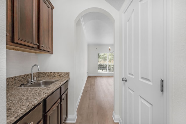 interior space featuring dark brown cabinetry, arched walkways, light wood-style flooring, light stone countertops, and a sink