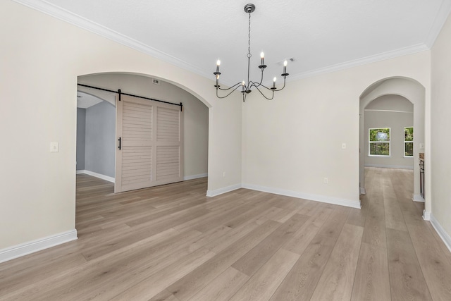 unfurnished dining area with light wood-style floors, arched walkways, crown molding, and a barn door