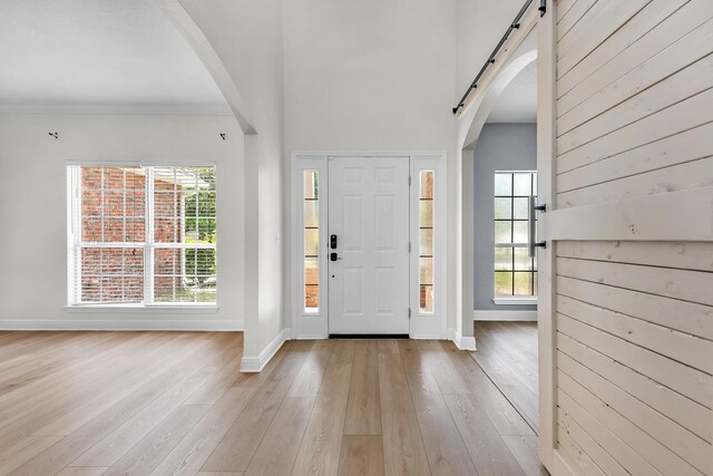 entrance foyer with light wood-type flooring, a barn door, and a towering ceiling