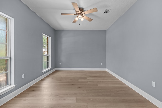 unfurnished room with ceiling fan, light wood finished floors, visible vents, and baseboards