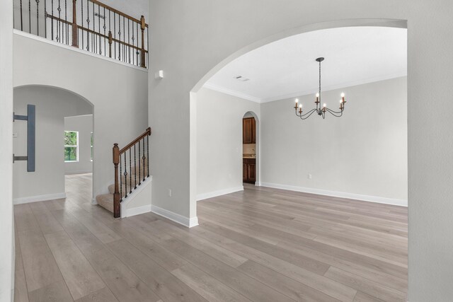 empty room featuring ornamental molding, a notable chandelier, light hardwood / wood-style floors, and a towering ceiling