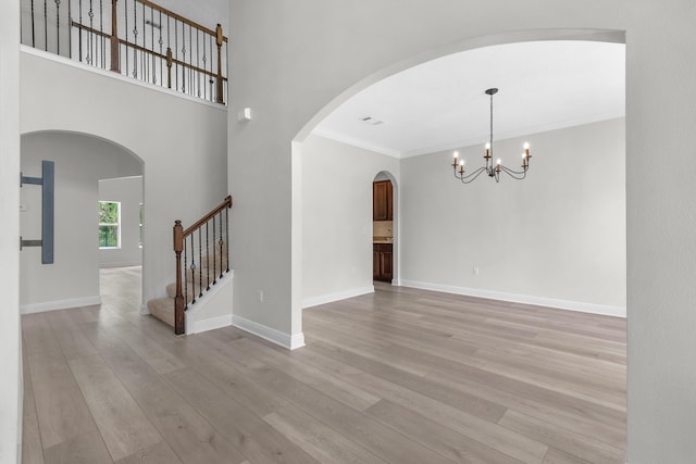 spare room featuring light wood-type flooring, crown molding, baseboards, and stairs