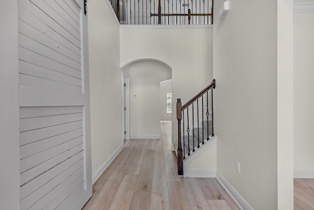 hall featuring light wood-style floors, a towering ceiling, baseboards, and stairs