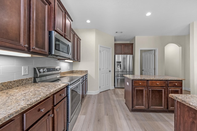 kitchen with appliances with stainless steel finishes, light hardwood / wood-style flooring, dark brown cabinetry, decorative backsplash, and light stone countertops