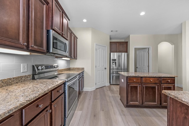 kitchen with arched walkways, stainless steel appliances, backsplash, light stone countertops, and light wood finished floors