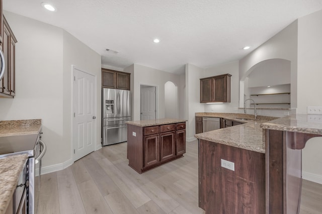 kitchen featuring light wood-type flooring, kitchen peninsula, stainless steel appliances, light stone countertops, and sink