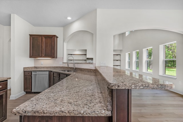 kitchen with light hardwood / wood-style flooring, dark brown cabinets, kitchen peninsula, dishwasher, and light stone countertops