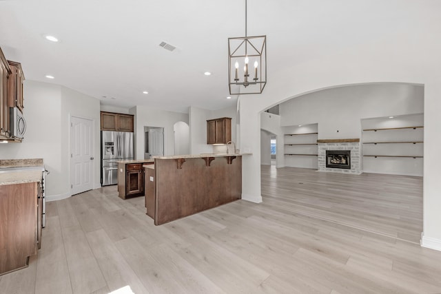 kitchen with stainless steel appliances, a fireplace, decorative light fixtures, light wood-type flooring, and a center island