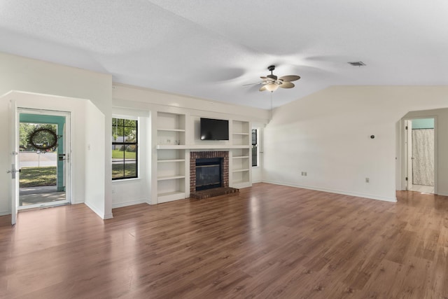 unfurnished living room featuring built in shelves, ceiling fan, wood-type flooring, and a brick fireplace