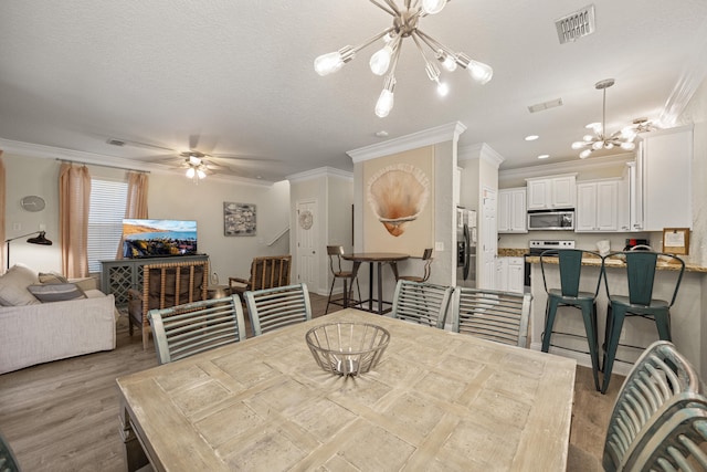 dining room featuring light hardwood / wood-style floors, a textured ceiling, crown molding, and ceiling fan with notable chandelier