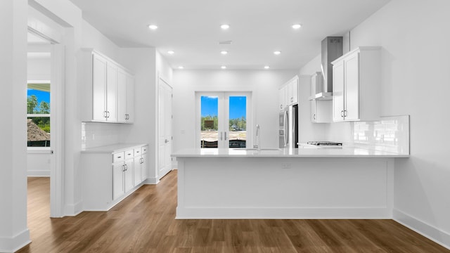 kitchen featuring wood-type flooring, tasteful backsplash, and wall chimney range hood