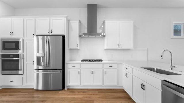 kitchen featuring light hardwood / wood-style flooring, stainless steel appliances, white cabinets, sink, and wall chimney exhaust hood