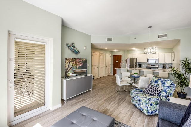 living area with light wood finished floors, visible vents, and an inviting chandelier