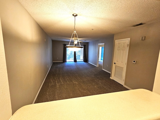 hallway with a textured ceiling and dark colored carpet