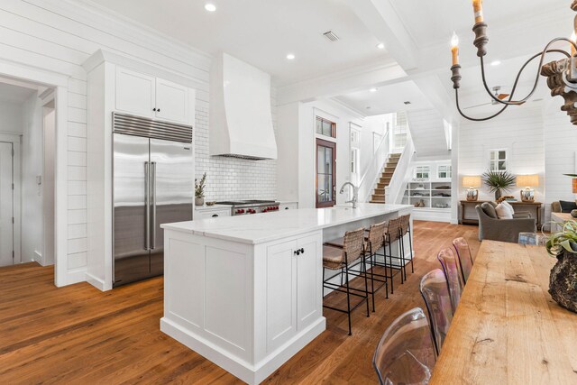 kitchen featuring tasteful backsplash, white cabinets, hanging light fixtures, light hardwood / wood-style floors, and built in refrigerator