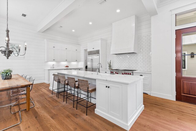 kitchen with a kitchen island with sink, built in fridge, light hardwood / wood-style flooring, and white cabinetry