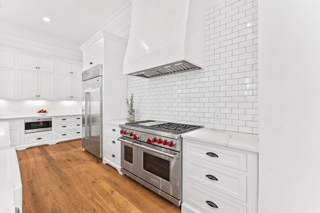 kitchen with white cabinets, premium range hood, light hardwood / wood-style floors, decorative backsplash, and high quality appliances