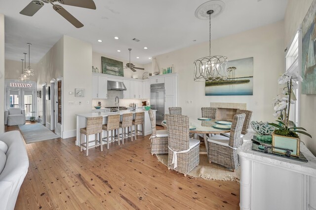 dining area with a high ceiling, sink, ceiling fan with notable chandelier, and light hardwood / wood-style floors