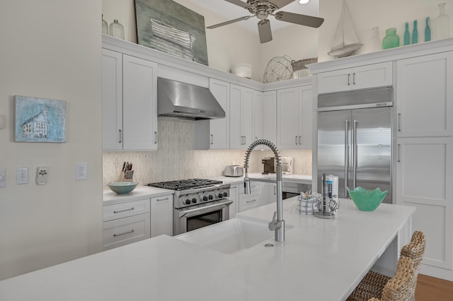 kitchen with high end appliances, backsplash, white cabinetry, and wall chimney exhaust hood