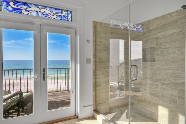 bathroom featuring a water view, a view of the beach, an enclosed shower, and french doors