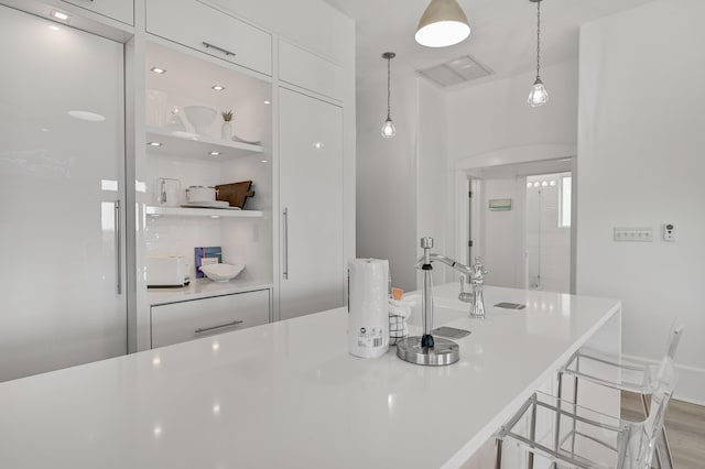 kitchen with white cabinets, a kitchen bar, hanging light fixtures, a center island, and light wood-type flooring