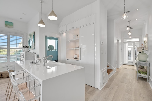 kitchen with hanging light fixtures, an island with sink, sink, and white cabinetry