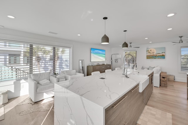 kitchen with a large island with sink, sink, pendant lighting, and light wood-type flooring