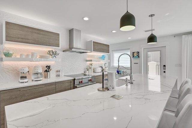 kitchen with stainless steel stove, tasteful backsplash, hanging light fixtures, light stone counters, and wall chimney range hood