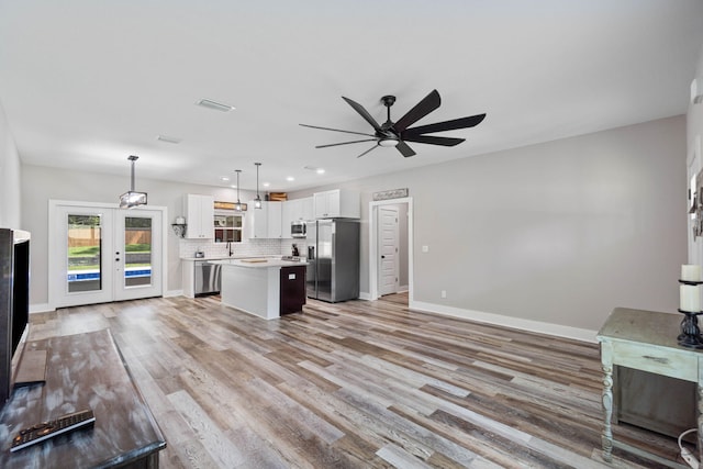 kitchen featuring appliances with stainless steel finishes, a center island, decorative backsplash, white cabinets, and decorative light fixtures