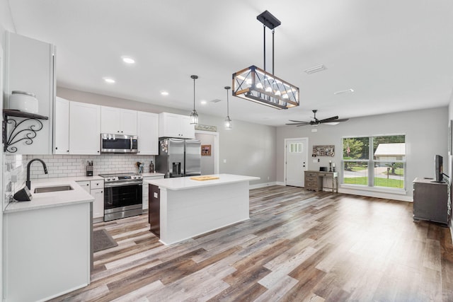 kitchen featuring sink, hanging light fixtures, a kitchen island, stainless steel appliances, and white cabinets