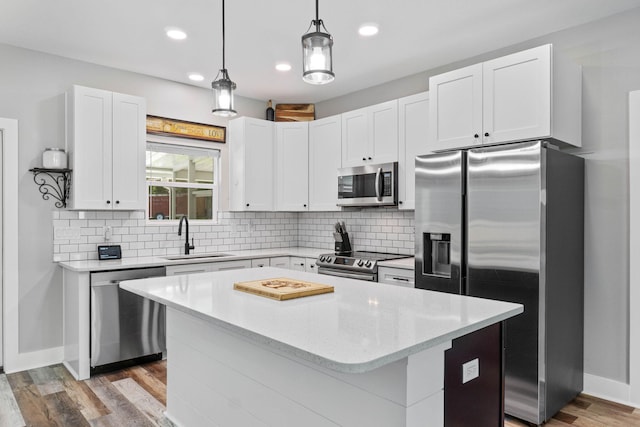 kitchen with pendant lighting, sink, stainless steel appliances, a center island, and white cabinets