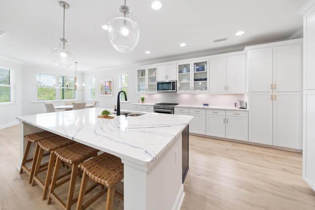 kitchen with light wood-type flooring, appliances with stainless steel finishes, decorative light fixtures, sink, and ornamental molding