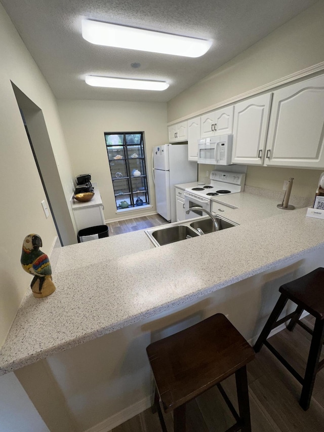 kitchen featuring white cabinetry, a breakfast bar area, kitchen peninsula, dark wood-type flooring, and white appliances