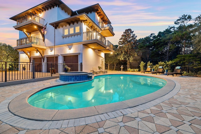 pool at dusk with a patio and an in ground hot tub