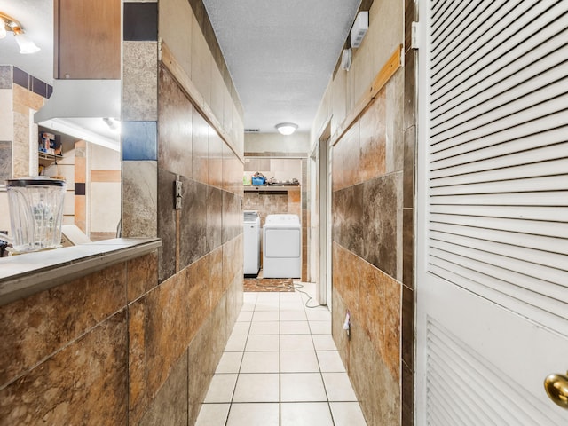 hallway with light tile patterned flooring, a textured ceiling, tile walls, and washing machine and clothes dryer