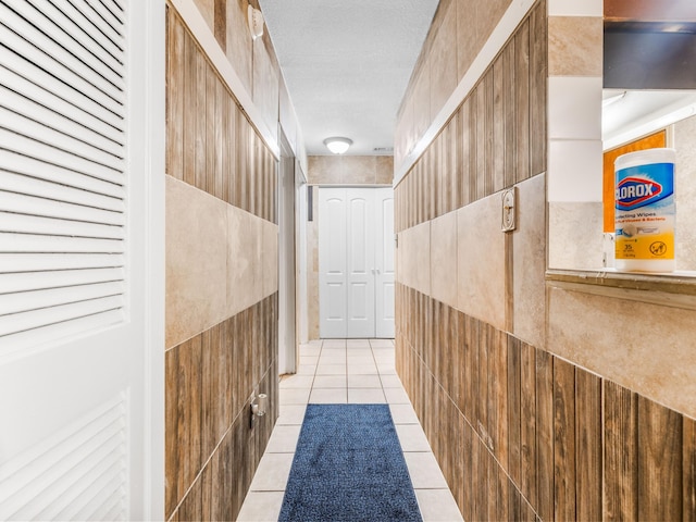 corridor featuring light tile patterned flooring, a textured ceiling, and tile walls