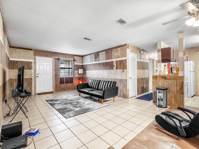 living room with wooden walls, light tile patterned floors, and ceiling fan