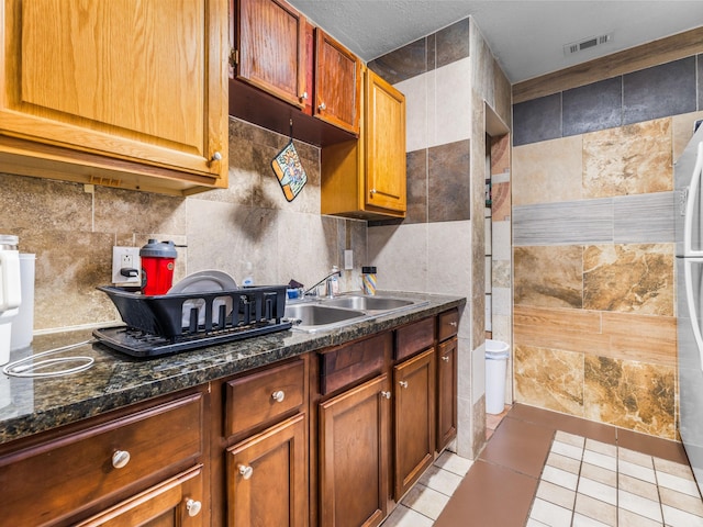 kitchen with sink, dark stone countertops, light tile patterned floors, and tile walls