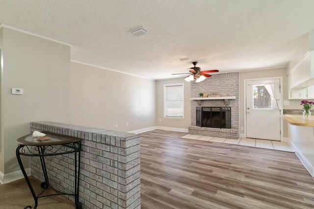 living room with crown molding, hardwood / wood-style flooring, ceiling fan, a textured ceiling, and a brick fireplace