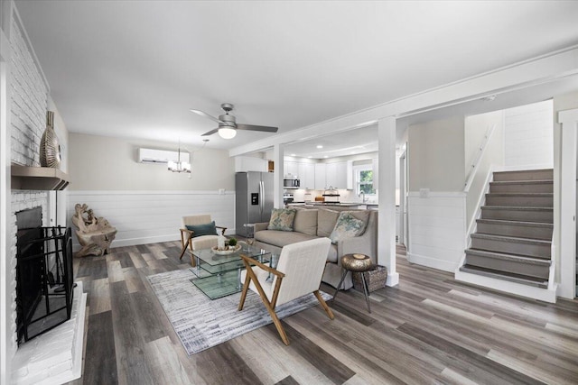 living room with ceiling fan with notable chandelier, a large fireplace, hardwood / wood-style floors, and an AC wall unit