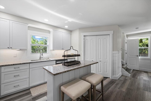 kitchen with light stone counters, sink, a kitchen island, and white cabinets