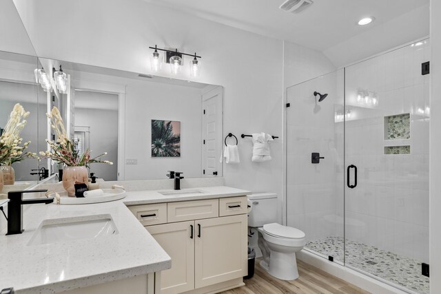 bathroom featuring a shower with shower door, wood-type flooring, double sink vanity, and toilet