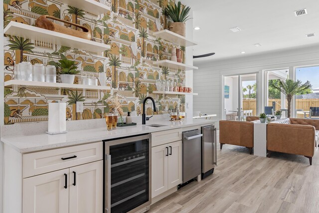 interior space featuring white cabinets, sink, light stone countertops, wine cooler, and light hardwood / wood-style floors